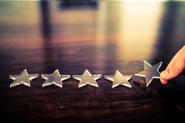 One more star The best rating. Businessman arranging five transparent stars in row on a wooden desk. The office window is reflected on the desk